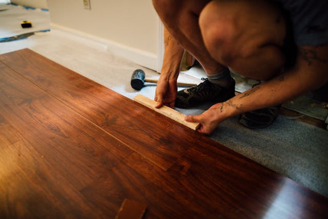 person-kneeling-while-installing-brown-flooring