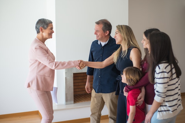 a-property-manager-in-a-pink-suit-shaking-hands-with-someone-who-is-standing-with-their-spouse-and-three-children a-property-manager-in-a-pink-suit-shaking-hands-with-someone-who-is-standing-with-their-spouse-and-three-children
