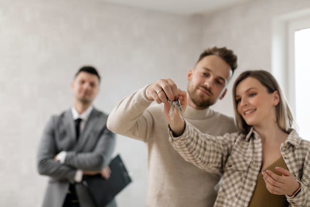 couple-looking-at-new-house-keys-while-property-manager-looks-on couple-looking-at-new-house-keys-while-property-manager-looks-on