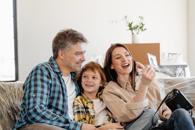 pexels-mart-production-7415122 two adults and a child laughing while sitting on a couch